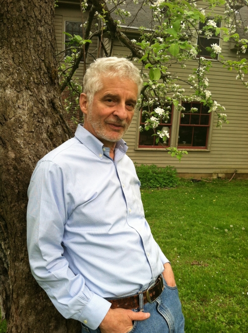 man in a blue button-up shirt leaning against a blooming tree